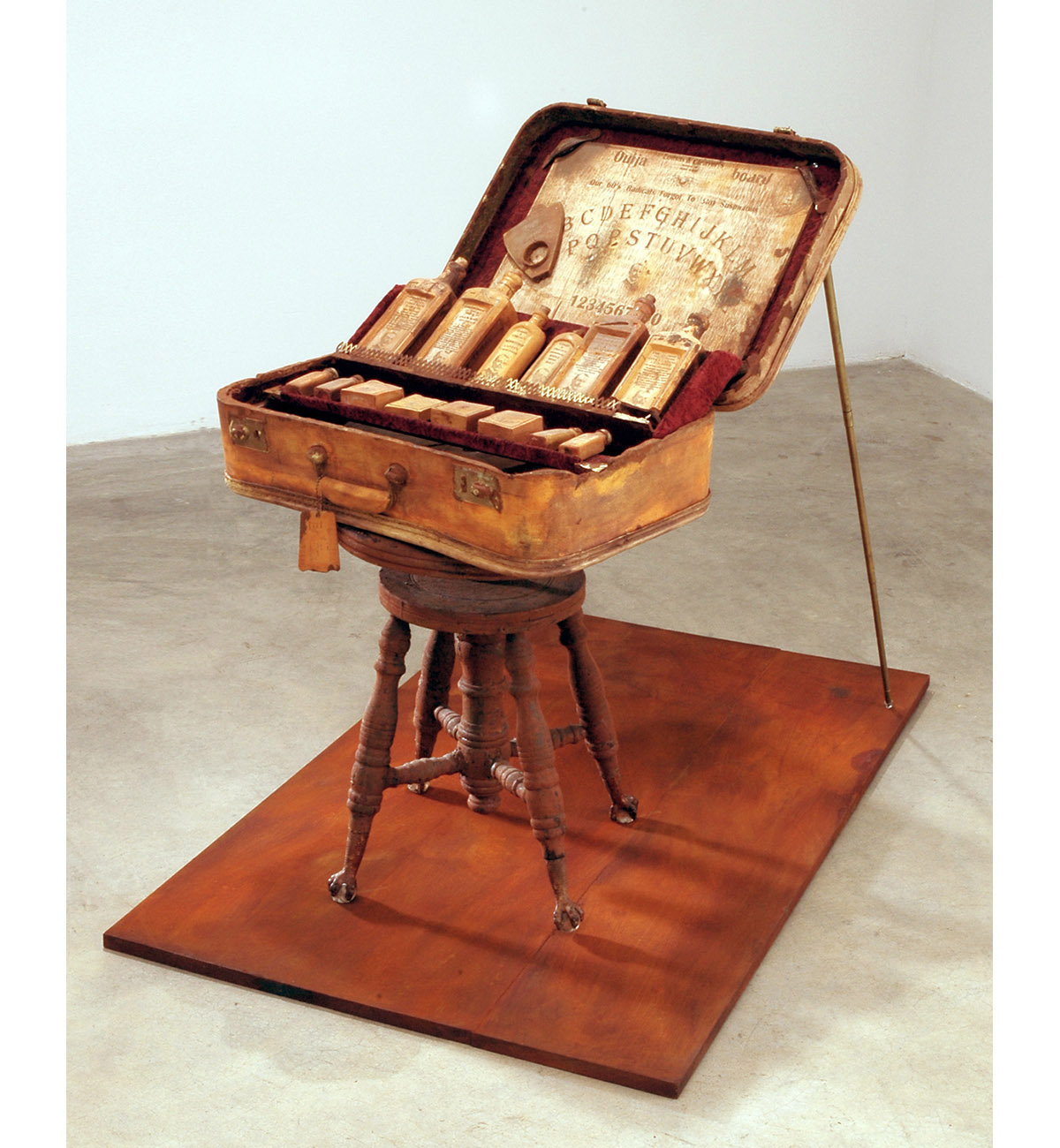 Dario Robleto
"Hippies And A Ouija Board (Everyone Needs To Cling To Something)", 2003-2004
Suitcase: cast and carved dehydrated bone calcium and bone dust from every bone in the body, microcrystalline cellulose, cold cast iron and brass, rust, antique syringe, crushed velvet, leather, thread, water extendable resin, typeset 
Bottles, medicines and Ouija board: cast and carved dehydrated bone calcium and bone dust from every bone in the body, typeset, homebrewed moonshine (potato derived alcohol), wine health tonics (water, sugar, fermented black cherries, yeast, gelatin, tartaric acid, pectinase, sulfur dioxide, oak flavoring, fortified with 100 year old: hemlock oil, Devil’s Claw, witch hazel bark, swamp root, powdered rhubarb, pleurisy root, belladonna root, white pine tar, coal tar, dandelion, sarsaparilla, mandrake, mullein, scullcap, cramp bark, elder, ginseng, horny goat weed, tansy, sugar of lead, mercury with chalk and tin-oxide; calcium, potassium, creatine, zinc, iron, nickel, copper, boron, vitamin k, crushed amino acids, home-cultured antibiotics, chromium, magnesium, colostrum, ironized yeast, ground pituitary gland, ground wisdom teeth, ground sea horse, shark cartilage, coral calcium, iodine and castor oil)
Records: various 1960’s 45 rpm records cast in prehistoric whale bone dust, typeset
23" x 19" x 42"
